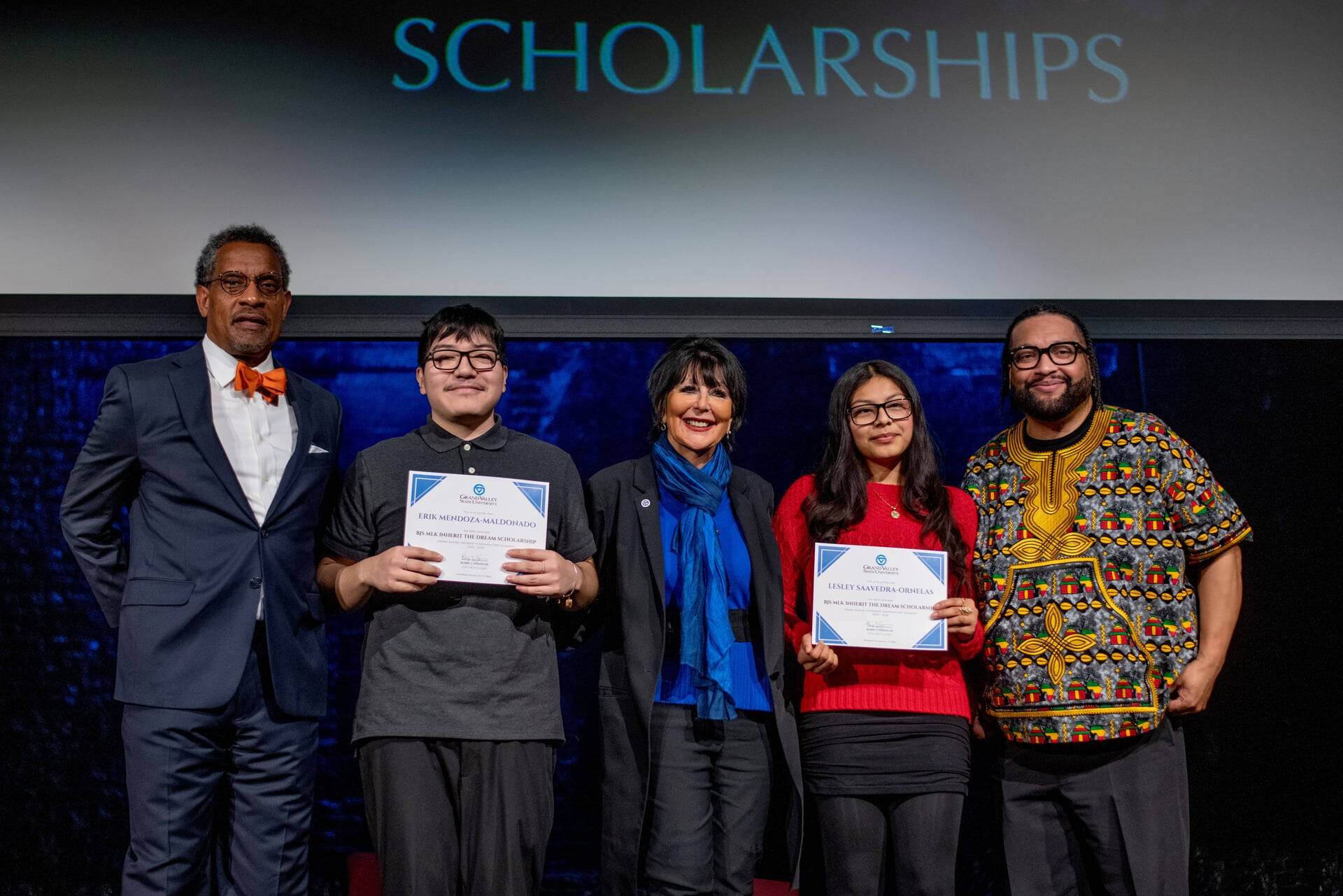 five people standing on stage, screen reads Scholarships, two students holding certificates